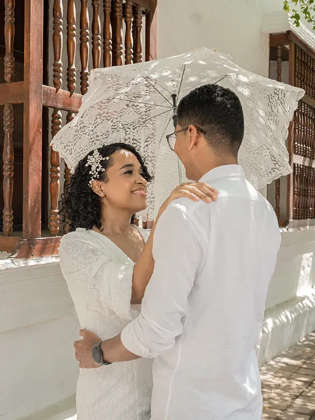 Brian y Lina bajo una sombrilla de encaje en un balcón de madera